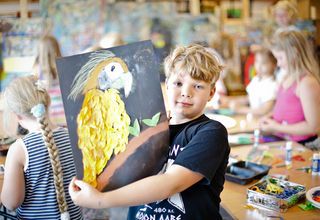 Chłopiec w czarnej koszulce trzyma pracę przedstawiającą żółtego ptaka