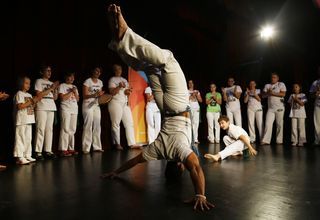 Mężczyzna stojący na głowie i chłopak obok, w tle młodzież