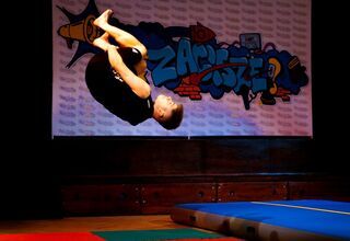 Chłopak w czarnym stroju wykonujący podczas akrobacji, pod nim kolorowe materace