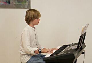Zdjęcie: Chłopiec w białej koszuli grający na pianinie elektronicznym