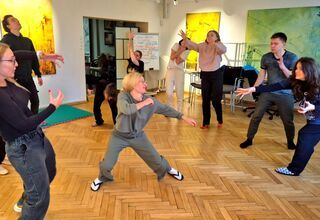 Zdjęcie: siedem kobiet i dwóch mężczyzn w ruchu, pokaz improwizacji na parkiecie, w tle kolorowe, duże obrazy