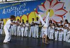Prezentacja sztuki walki na scenie, w tle młodzież ubrana  na biało i kolorowy baner Artystyczny Targówek