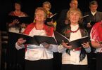 Cztery kobiety z chusatmi ludowymi oraz dwóch mężczyzn w garniturach, śpiewający ze śpiewniczków