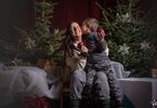 Matka z dzieckiem pozująca do zdjęcia na świątecznym tle w formie choinek z lampkami, prezentów, siedząca na świątecznym fotelu i pufach DK Zacisze