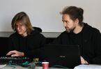 Dwóch mężczyzn w czarnych bluzach przed laptopem i stołem akustycznym