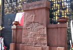 Czerwony pomnik Dmowskiego, z boku powiewa flaga biało-czerwona