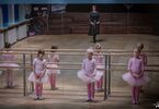 Trzy dziewczynki w strojach baletowych i kobieta przed nimi na parkiecie
