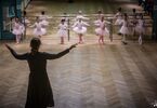 Kobieta z rozłożonymi rękoma pokazuje pozę taneczna dziewczynkom w strojach baletowych