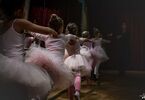 Dziewczynki stoją tyłem z uniesioną nogą i ręką w pozie baletowej