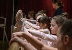 Dziewczynki z nogą opartą o drążek baletowy, w tle instruktorka