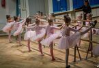 Dziewczynki w różowych strojach w pozie baletowej przy drążku