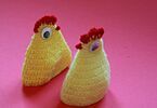 Dwa żółte kurczaki wykonane na szydełku na różowym tle