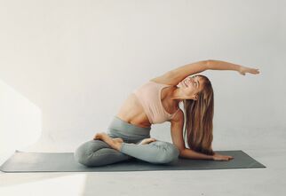 Kobieta na macie gimnastycznej w pozycji lotosu z wyciągniętą prawą ręką