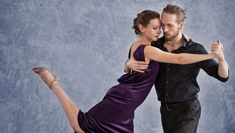 Zdjęcie: młoda kobieta i młody mężczyzna w pozycji tanecznej, kobieta ma nogę podniesioną do góry, szare tło